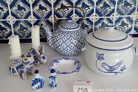 Full set of vintage blue and white items on counter with tile background: teapot with brass handle, covered crock with bird design, Shelley Dainty Blue ashtray, two rabbit candleholders holding white candles, two small blue and white Asian-style perfume bottles.