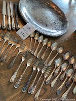 Full overview of vintage silverplate flatware including knives, forks, spoons, and large round tray on a wooden surface showing overall set condition and arrangement.