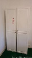 Front view of tall white cabinet with two closed paneled doors and brass handles.