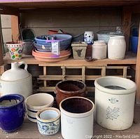 Wide view showing various ceramic pots, crocks, planters, and stacked trays on wooden shelves including Red Wing jug
