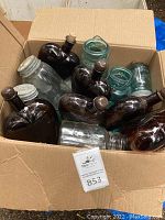 Box containing a mix of brown glass heart-shaped bottles, clear glass jars with metal lids, and blue Ball jars with wire spring tops.