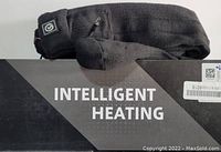 Close-up photo showing a pair of black heated socks laid on their packaging box which features the text 'INTELLIGENT HEATING'.