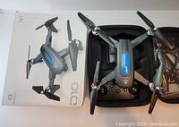 The photo shows the DeerC D10 drone unfolded alongside its remote controller, spare propellers, and original packaging box. The drone and accessories are arranged on a flat surface along with a carrying case.