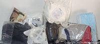 Photo showing various face masks and accessories including KN95, blue paper masks, cloth masks with filters, black lined masks, camo masks, black stretchy masks, fashion masks, plastic mask brackets, and black single layer masks all in sealed packs.