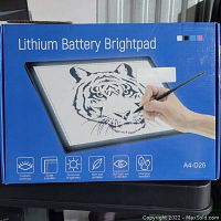 Front of blue box showing Lithium Battery Brightpad light box with a hand tracing a tiger image on illuminated surface.