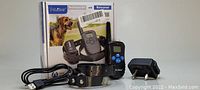 Photo showing all contents of the pet training collar system including the box, remote transmitter, receiver collar on black dog collar, USB cable, and charging dock.