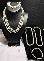 Display of 3 pearl necklaces with sterling silver clasps; 2 pearl bracelets with sterling silver clasps; and 3 pairs of pearl earrings with sterling silver studs arranged on a black display and white surface.