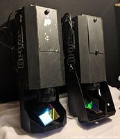 Two black metal American DJ Orbit II lighting fixtures showing prism glass lenses and mounting brackets, with visible wear and scuffs on housings.