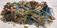 Photo of a large pile of assorted broken jewelry pieces including beads, chains, and bracelets in various colors and materials.