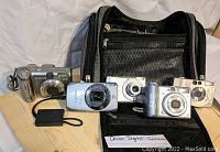 Four Canon digital cameras with camera bag and battery accessories arranged on a table, showing variety in size and model.