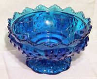 Front angled photo showing the blue hobnail glass candle holder with scalloped edge and pedestal base.