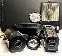 Front view of six DJ lighting equipment units showing various branded devices mostly black metal housings with lenses and ventilation grilles.