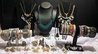 Photo showing a wide assortment of rhinestone bracelets, necklaces displayed on busts, rings, brooches, and pendants arranged on a white surface and black stands.