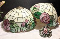 Three stained glass lamp shades displayed together showing floral patterns and sizes