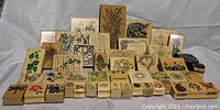 Photo shows 47 wooden stamps with carved floral and insect designs arranged in rows on a white surface.