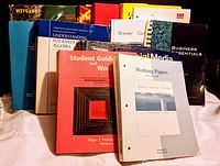 Photo showing multiple textbooks and manuals standing upright, titles readable such as Intermediate Algebra, Business Essentials, Social Media, among others.