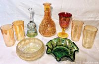 Full lot of 9 carnival glass pieces grouped on white cloth background, showing all items in the collection for sale.