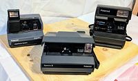 All three Polaroid cameras displayed on wooden surface showing front view and built-in flash units.