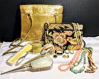 Full lot showing gold sequin handbag, floral tapestry handbag, silver-plated comb, brush, mirror set, and jewelry with beaded necklaces.