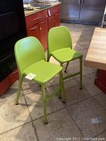 Pair of green Urban IKEA kids dining chairs positioned in a kitchen setting showing front and side views