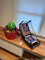 Franklin basketball game alongside red bucket holding sports balls including a green soccer ball and tennis ball