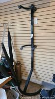 Full view of black metal bicycle stand mounted on wall, showing vertical support bar and top adjustable hooks.