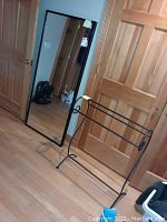 Black metal blanket rack next to black framed Ikea Stave mirror standing on the floor against a wooden door