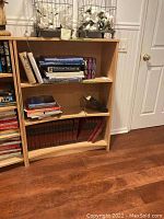 Front view of wooden bookcase filled with books illustrating three shelves with various book sizes and colors.