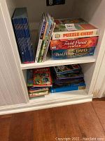 Shelves with boxed board games Puzzle Chest, Trivial Pursuit Junior, Trivial Pursuit DVD Pop Culture, and assorted children's books including Pokemon and Scholastic.