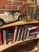 Side view of a bookshelf showing various books including history and fiction titles with a model car and lantern on upper shelf.