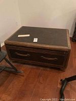 Front-side angled photo showing rectangular coffee table with dark brown textured leather top and drawer with leather strap handles.