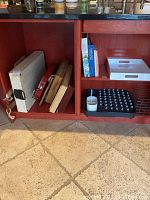 Wide view of cabinet shelves containing cutting boards, cookbooks, trays including silverware tray, red serving tray, and white trays for dishes.
