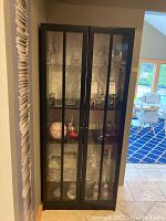 Front view of black wooden display cabinet showing glass doors and contents inside.