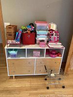 Photo of assorted children's toys including Disney princess dolls, wicker baskets, plastic containers, karaoke machine, and storage unit.