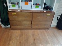 Full view of a medium brown wooden dresser with four drawers and metal pulls on each drawer, placed on wooden floor with some items on top.