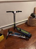 Two foldable electric scooters placed on wooden floor indoors, one upright and one folded.