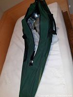 Green fabric carry bag partially unzipped to show fencing gear inside