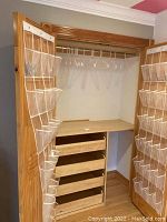 Wide angle photo showing two shoe organizers hanging on door frames inside a closet with multiple clear pockets and several plastic hangers on a closet rod