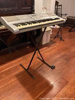 Side angled view of Yamaha keyboard on metal X-style stand showing keyboard and stand details.