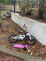 Side view of white Cannondale kids bike and pink Micro scooter on leaf-covered ground outdoors.