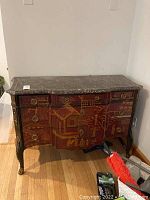 Front view showing serpentine drawer arrangement, red lacquer chinoiserie decoration, brass ring pulls, and marble top.