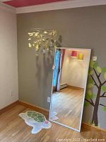 Photo showing the mirror leaning against a wall with the turtle-shaped rug on the floor and the yellow flower mobile hanging above, capturing all three items in use context.