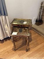 Stacked view of two matching wooden nesting tables with carved cabriole legs and aged decorative tops showing wear and tear.