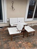 Frontal view of two-seat bench and side table on brick patio against house wall