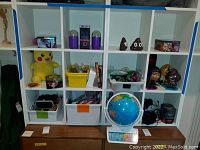 Wide shot of 12 cubbies containing various toys and collectibles including Pokemon Plush, figurines, and bins with small items, plus an interactive globe on the table.