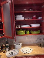 Open kitchen cabinet shelf showing white and red bakeware, green and polka dot ceramic bowls