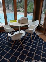 Full view of the tulip-style table surrounded by four white molded plastic chairs with wooden legs on a patterned rug, showing overall condition and setup.