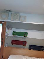 Photo showing all three train shaped wall shelves mounted on the wall in green, red and blue colors, along with the moon light to the left and three framed circular art pieces above.