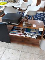 Photo of a wooden coffee table holding a closed dark typewriter case with a handle, two silver-tone crystal decorations, and three large coffee table books beneath.