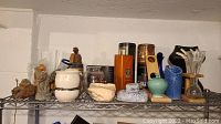 Wide view of shelf with assorted vases, figurines, tins, and planter showing layout and item types
